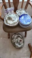 Several winter design serving platters and blue winter plates stacked on a chair, plus one platter on floor