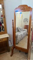 Full view of the standing mirror with wooden frame reflecting a sofa and wall decor in the background.