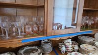 Glass cabinet displaying a variety of glassware including etched stemware with floral and hummingbird designs.