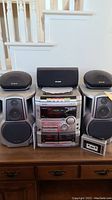Full view of the Aiwa stereo system with stereo main unit, two large stereo speakers, two smaller satellite speakers, center speaker, and cassette tape in front