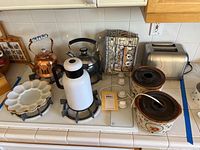 Full view of all items on kitchen counter including toaster, teakettles, thermos, deviled egg plate, and potpourri crocks