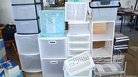 Overall view showing multiple plastic storage bins with drawers and rollers, assorted baskets, and a shower rack.