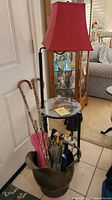 Full view of the glass top table with a red lampshade lamp and the bucket with walking canes and umbrellas.