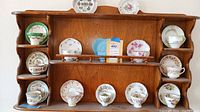 Full view of oak wall shelf with twelve tea cup and saucer sets on ledges and cubbies