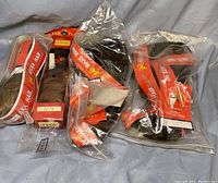 Several packaged wigs in sealed clear plastic bags with red orange Maxx Hair branding and text indicating 100% human hair and Style J-C-Curl synthetic. Different bundles of dark hair inside.