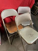 Front view of three metal folding chairs, one with wood seat and two with metal seats and backs, showing wear and surface scratches.