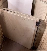 Photo of the folded 5-foot banquet table showing the white tabletop with some marks and stains, stored upright against a wall.