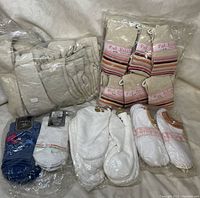 Multiple packages of new socks arranged on a fabric surface showing various colors and styles including beige quilted, striped Pink Bubbles socks, white ankle socks, and a blue pair with a flamingo design.
