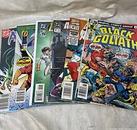 Seven comic books arranged side by side showing front covers of each. Titles include Black Goliath, Fantastic Four, Alpha Flight, Batman, Aquaman.