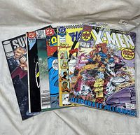 Photo showing front covers of a stack of seven assorted comic books including Uncanny X-Men, Thundercats, and DC/Marvel titles.