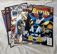 Seven comic books stacked fanned out showing front covers, featuring Batman prominently and several Marvel titles.