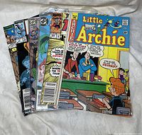 Five comic books arranged in a slight fan showing front covers. Titles include Little Archie and several Marvel Comics issues featuring characters like Thor.