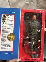 Front view of unopened action figure in original red and blue window display box. Figure dressed in WWII military uniform with accessories visible.