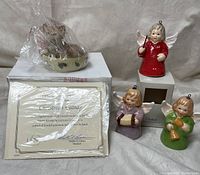 Lenox Christmas Catnap figurine and three Goebel angel bell ornaments placed on a white surface with some items wrapped in plastic.