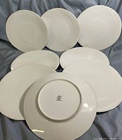 Set of eight white Lenox Origins pattern porcelain dinner plates arranged in two rows on a gray fabric background, one plate flipped to show the backstamp.