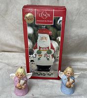 Front view of two Goebel angel bell figurines in lavender and blue holding harps, with Lenox Santa Claus pepper mill box behind