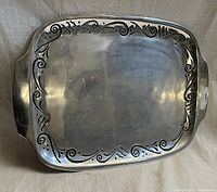 Top view of Lenox Spyro Holloware rectangular metal serving tray showing decorative scroll border and integrated handles with some surface wear.