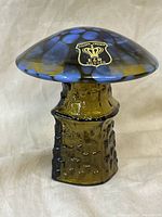 Front view of hand blown glass mushroom showing textured amber stem, blue-yellow spotted cap, and original Golden Crown E & R Sweden label