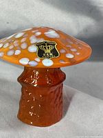Side angle showing orange textured glass stem and underside of spotted orange cap with Golden Crown E & R Sweden label attached.
