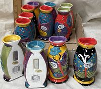 Twelve ceramic magnetic vases grouped in open cardboard box showing fronts and backs of pieces, highlighting colorful designs and magnetic backs with Ganz branding labels.