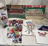 Image showing assortment of Phillies memorabilia including team photos, player cards, booklets, and bobblehead figurine