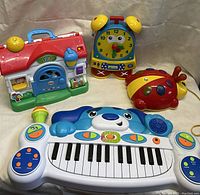 Four colorful children's educational toys including a playhouse, clock, ladybug, and electronic keyboard.