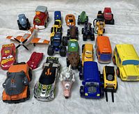 Overview photo of 22 assorted toy vehicles including cars, trucks, dinosaurs, and planes arranged on a white sheet.