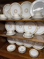 Photo showing multiple stacks of plates, saucers, and cups in Harvest pattern on wooden shelves.