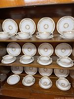 33-piece Narumi China set from 1940s Occupied Japan, Harvest pattern. Includes 12 saucers, 11 double-handled broth cups, 12 salad plates arranged on wooden shelves.