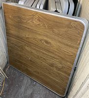 Photo showing the woodgrain top and metal edging of the folded table stored upright.