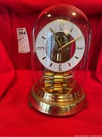 Full view of vintage anniversary clock under glass dome showing brass finish base and pendulum, white clock dial with black numbers.