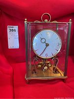 Front view of vintage anniversary clock with brass frame, glass sides, white clock face with gold numbers, and rotating pendulum inside