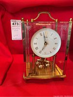 Vintage anniversary clock with brass finish inside a glass and brass dome, showing full front view with red background.