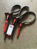 Three Husky band wrenches photographed on concrete floor, showing the front view of handles and metal bands