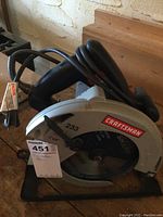 Craftsman 7 1/4 inch circular saw placed on wooden surface showing the left side, power cord coiled on top, and product identification tag attached.