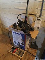 Dremel rotary tool placed in its original box alongside a wooden attachment box on a wooden surface next to a wall.
