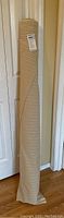 Full length view of the fabric roll standing upright, showing the beige color and visible striped pattern.