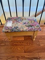 Front view of foot stool showing floral upholstered cushioned top and light wood legs.