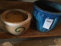 Photo of two gardening pots side by side; one large blue ceramic pot and one smaller beige ceramic pot with green swirl.