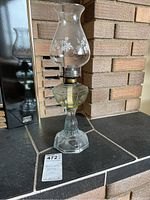 Full view of the glass kerosene lamp showing the chimney with floral patterns and glass base.
