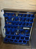 Full view of the metal frame hardware storage organizer with blue plastic bins on wall.