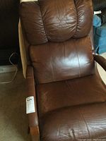 Front view of brown leather recliner showing cushioned headrest, back, and padded armrests with wood trim