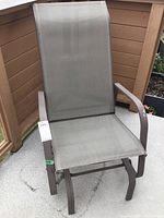 Full view of patio rocker chair showing brown metal frame and beige mesh fabric seat and backrest.
