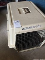 Photo showing front metal wire mesh door of the beige Kennel Cab plastic pet carrier with label and top handle.