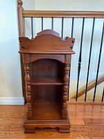 Full view of the wooden plant stand showing two shelves and turned posts on the front sides, with scalloped trim on the top and base.