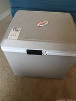 Front view of the light gray plastic electric cooler with black latch and label on lid.