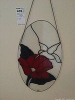 Full view of the oval stained glass wall hanging showing the red flower, white petal detail, and dark leaves with hanging chain