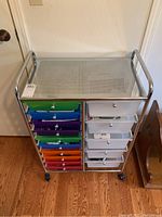 Full front view of metal storage unit showing colorful and translucent white plastic drawers organized in columns, unit is on wheels.