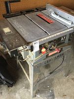 Craftsman table saw with visible control knobs, power cord, and metal stand, showing 'CRAFTSMAN' on the table surface.