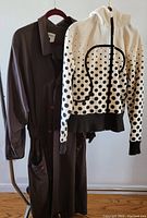 Photo showing long brown nylon coat by Plantation with button closures and white polka dot zip hoodie by Lulu Lemon hanging on rack.